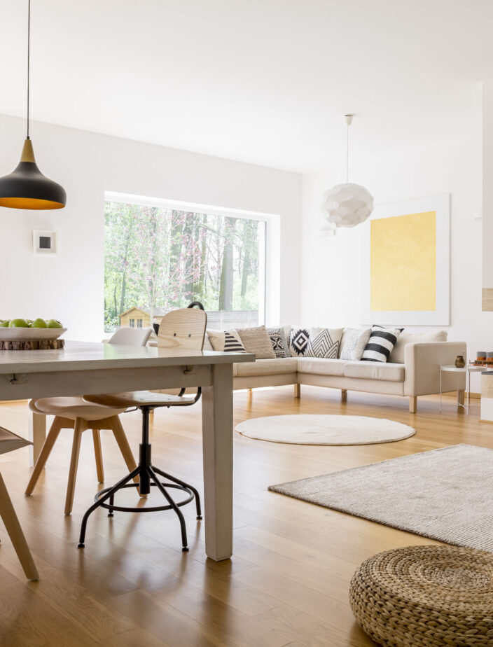 Black designed lamp above dining table in spacious living room with braided pouf on wooden floor